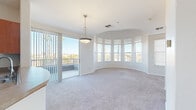Located at 9680 W Northern Ave in Peoria, Arizona, this well-appointed 2-bedroom, 2-bathroom single-floor residence offers a thoughtfully designed layout with notable architectural character. The standout feature is the striking curved living room, defined by a sweeping arc of large windows that flood the space with natural light and frame views of the surrounding Arizona landscape. A sliding glass door opens to a private balcony, seamlessly connecting indoor and outdoor living. Soft carpeting and a pendant light fixture complete the living area's inviting ambiance. The galley-style kitchen features warm wood cabinetry, a tile backsplash, hardwood-style flooring, and a breakfast bar pass-through that connects to the entry hallway. Arched doorways lend an elegant architectural touch throughout the transitional spaces. The primary bedroom is generously sized and showcases its own curved bay window arrangement with a ceiling fan, while a walk-in closet with built-in wire shelving provides ample storage. The second bedroom also offers a ceiling fan and natural light. Both bathrooms are finished with wood-toned vanities and hardwood-style floors. A second carpeted walk-in closet adds further storage convenience. The layout flows efficiently through a central hallway connecting all rooms.