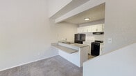 This two-story residence is efficiently designed across two floors, offering a well-organized layout that maximizes functionality. The main floor hosts the combined kitchen and living area, where soaring ceilings create a sense of openness well beyond the physical footprint. The kitchen is thoughtfully appointed with white shaker-style cabinetry, light speckled countertops, a double stainless steel sink, wood-look vinyl flooring, and black appliances including a gas range, refrigerator, and dishwasher. A peninsula counter connects the kitchen to the carpeted living area, providing additional workspace and a natural divider between the two zones. The main floor also includes the full bathroom, which features a single-sink vanity with speckled countertop, a large mirror, wood-look flooring, and a tiled shower-tub combination. Ascending the staircase leads to the upper-floor bedroom, a cozy and private retreat carpeted throughout with a window that invites natural light and outdoor views. The bedroom also features a built-in closet with shelving for organized storage. Neutral tones, textured ceilings, and clean white walls carry throughout the home, lending a cohesive and move-in-ready aesthetic to the entire space.