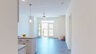 Located at 15000 Penmon Dr in Fuquay-Varina, NC, this well-appointed one-bedroom, one-bathroom unit offers a thoughtfully designed layout across a single floor. The open-concept kitchen and living area serves as the heart of the home, featuring light wood-style flooring, crisp white walls, and abundant natural light. The kitchen is equipped with stainless steel appliances — including a refrigerator, electric range, and dishwasher — complemented by granite countertops, white cabinetry with matte black hardware, a peninsula with a sink, and pendant lighting overhead. A wall-mounted range hood adds a contemporary touch. The living area flows effortlessly toward a glass-paneled door that opens to a private balcony, offering outdoor views of the surrounding neighborhood. A ceiling fan overhead enhances comfort throughout the space. The bedroom is a calm retreat finished with plush carpet flooring, dual windows that bring in generous daylight, and a ceiling fan. It connects directly to a walk-in closet outfitted with wire shelving and hanging rods, providing ample storage. The full bathroom features wood-style flooring, a tub-shower combination, and built-in shelving. A connecting hallway ties the private spaces together seamlessly, completing this clean and modern home.