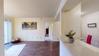 Located at 6942 E Rosewood St in Tucson, Arizona, this single-story residence offers a functional and well-organized layout throughout. The main living area features rich, dark hardwood-style flooring that extends through the open space, complemented by neutral walls and a textured ceiling. A half-wall with a light stone-finish countertop separates the living area from the kitchen, creating a natural division while maintaining an open feel.

The galley-style kitchen is equipped with warm wood cabinetry, white appliances including a range and full-size refrigerator, a stainless steel sink, and light countertops. An adjacent open shelving nook provides additional storage and organizational convenience.

The residence includes two bedrooms, both finished with plush carpeting and ceiling fans with light fixtures. The primary bedroom connects directly to a private bathroom, while a second bedroom features a window that allows natural light to fill the space. The bathroom is outfitted with a full tub and shower combination and built-in open shelving along one wall, offering practical storage.

Overall, the home presents a clean, straightforward design with consistent finishes throughout, making it a practical and comfortable space in a well-established Tucson neighborhood.