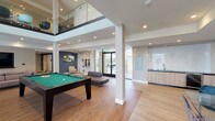 Located at 119 N Pacific Ave in Glendale, California, this contemporary amenity lounge is thoughtfully designed to offer a variety of social and recreational spaces within a single, open floor plan. The space is characterized by clean architectural lines, light wood-look flooring, and a neutral color palette accented by deep teal walls that add visual depth throughout.

The main gathering area centers around a full-size billiard table and is flanked by comfortable lounge seating, including a large sectional sofa paired with a glass coffee table and a wall-mounted flat-screen television — ideal for casual gatherings. An upper-level glass railing overlooks this central zone, adding a sense of vertical openness and architectural interest.

A dedicated dining area features glass-top tables and upholstered chairs set against a striking marble-effect feature wall with an inset television screen. Natural light filters in through large windows, enhancing the refined ambiance.

The kitchen is fully equipped with stainless steel appliances, including a French door refrigerator and built-in oven, warm wood cabinetry, dark stone countertops, and a marble-style backsplash. A separate, more intimate seating nook with a leather sofa and floor-to-ceiling windows rounds out the versatile layout.