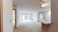 Located at 1060 N 115th St in Wauwatosa, Wisconsin, this well-appointed two-bedroom, two-bathroom residence offers a comfortable and functional single-floor layout. The combined kitchen and living room serves as the heart of the home, with the kitchen featuring warm oak cabinetry, ample counter space, and white appliances including a refrigerator, electric range, and dishwasher, set atop easy-care tile flooring. The living room extends from the kitchen and is bathed in natural light through a large sliding glass door that opens onto a private balcony. The balcony is framed by a distinctive brick pillar and white metal railing, offering serene, tree-lined views that provide a sense of natural seclusion. Both bedrooms are generously proportioned, featuring neutral carpet and clean white walls with warm wood baseboards and trim throughout. The primary bedroom is notably spacious, providing ample room for a full suite of furnishings. The two bathrooms are finished with tile flooring, wood-toned vanity cabinetry, and full tub and shower combinations. A connecting hallway ties the layout together efficiently. The overall ambiance is clean, bright, and move-in ready, with a calm, residential character enhanced by the lush green surroundings visible from multiple rooms.