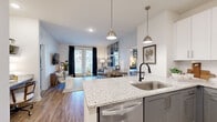 Located at 3355 Club Dr in Lawrenceville, Georgia, this single-floor residence offers a thoughtfully designed open-concept layout with modern finishes throughout. The kitchen is a standout feature, showcasing granite countertops, a large center island with bar seating, two-tone cabinetry with gray lower and white upper cabinets, stainless steel appliances including a refrigerator, range, and built-in microwave, and sleek pendant lighting. The kitchen flows seamlessly into the living area, which is bright and welcoming, with wood-style flooring, recessed lighting, and French doors that invite natural light and provide access to an outdoor area. A shiplap-style accent wall adds a contemporary touch to the living space. The bedrooms are carpeted and well-sized, each featuring large windows with views to the exterior, ceiling fans, and distinct design accents — one with striped wallpaper and another with a soft sage green accent wall. Each bedroom is complemented by a walk-in closet outfitted with wire shelving systems, offering generous storage capacity. The overall ambiance of the residence is clean, bright, and modern, with a cohesive neutral palette accented by thoughtful design details throughout.