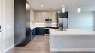Located on East Colfax Avenue in Denver, Colorado, this modern one-bedroom, one-bathroom residence offers a thoughtfully designed open-concept layout finished with contemporary details throughout. Light wood-tone flooring runs across the entire space, lending warmth and visual continuity from room to room.

The kitchen is a standout feature, showcasing a large island with a white quartz countertop, undermount sink, and pendant lighting above. Two-tone cabinetry pairs navy blue lower cabinets with light wood upper cabinets, complemented by a white subway tile backsplash and a full suite of stainless steel appliances, including a refrigerator, range, microwave, dishwasher, and a built-in wine cooler. The kitchen flows seamlessly into the living area, which opens to a private balcony offering outdoor views of surrounding tree canopies.

The bedroom is generously sized, bathed in natural light through a large picture window with scenic treetop views, and equipped with a ceiling fan. Two closets and a hallway provide ample storage throughout the unit.

The bathroom features a sleek, dark-framed glass walk-in shower with large-format tile surround, a white quartz vanity, and matte black hardware accents. An in-unit laundry area adds everyday convenience. The overall ambiance is clean, modern, and inviting.
