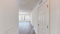 Located at 240 Yoakum Pkwy in Alexandria, Virginia, this one-bedroom, one-bathroom residence offers a thoughtfully organized single-level layout with a clean, modern aesthetic. The combined kitchen and living room area forms the heart of the home, where light wood-tone flooring runs throughout and large windows dressed with vertical blinds invite abundant natural light and views of the surrounding greenery. The kitchen features dark granite countertops, white shaker-style cabinetry with brushed nickel hardware, stainless steel appliances — including a refrigerator, range, and dishwasher — and a pass-through window that connects seamlessly to the living area, enhancing the open feel of the space. The spacious primary bedroom is finished with plush carpeting and its own large window, creating a comfortable and well-lit retreat. A dedicated walk-in closet with dual wire shelving provides generous storage. The full bathroom is finished in crisp white tones with a tub-shower combination, a single-sink vanity with white cabinetry, and wood-look flooring that ties the space together. A textured ceiling and neutral white walls throughout contribute to the bright, airy ambiance of this efficiently designed Alexandria residence.