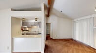 This single-story home offers a thoughtfully designed layout that balances comfort and functionality throughout. The living area makes an immediate impression with soaring vaulted ceilings accented by exposed wooden beams, creating a sense of openness and architectural character. A brick fireplace with a raised tile hearth and classic white mantel serves as a focal point in the living room, complemented by a sliding glass door that allows natural light to filter in through vertical blinds.

The kitchen is efficiently designed in a galley-style layout, featuring gray-toned cabinetry with decorative detailing, light stone-look countertops, a stainless steel double-basin sink, a white electric range, and a stainless steel refrigerator. It opens to the living area via a pass-through breakfast bar with wainscoting detail, making the space feel connected and social. Light tile flooring runs throughout the kitchen.

The bedrooms are carpeted and offer generous closet space with sliding doors, and each provides convenient access to a bathroom. The bathrooms are clean and functional, featuring stone-look countertop vanities, framed mirrors, and tub-shower combinations with tile flooring. A notable convenience is the in-unit washer and dryer, accessible directly from one of the bathrooms, adding everyday practicality to the home's overall well-considered design.