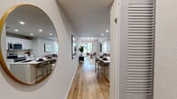 Located at Natura Gardens in Hialeah, FL, this single-floor residence offers a thoughtfully designed open-concept layout with contemporary finishes throughout. Light wood-style flooring flows seamlessly from the welcoming entryway — accented by a round mirror and louvered closet door — into the expansive living, dining, and kitchen areas. Recessed lighting and large windows invite abundant natural light, enhancing the bright, airy ambiance of the main living space. The kitchen is well-appointed with crisp white cabinetry, white quartz countertops, stainless steel appliances including a refrigerator with ice maker, electric range, and microwave, plus a center island with bar seating. The dining area features a sliding glass door that opens directly to a private outdoor patio with garden views. The living room is connected to the bedroom wing, where well-proportioned bedrooms offer comfortable retreats with large windows and neutral tones. The bathroom features marble-style tile surround in the shower/tub combination, a white vanity, and wood-look flooring. Throughout the residence, a cohesive modern aesthetic is maintained with neutral walls, bold artwork accents, and quality fixtures, creating a polished and functional living environment.