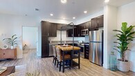 Located at 7847 Mission Gorge Rd in Santee, California, this single-story unit offers a thoughtfully designed layout with contemporary finishes throughout. The kitchen serves as a functional centerpiece, featuring dark espresso cabinetry, stainless steel appliances including a gas range, built-in microwave, and full-size refrigerator. A freestanding butcher block island with an overhead metal rack and woven bar seating adds both character and utility to the space. Wood-look luxury vinyl flooring runs continuously through the unit, providing a warm and cohesive aesthetic. The multiple bedrooms are bright and inviting, each featuring large double-hung windows that frame views of the surrounding greenery and neighborhood landscape, flooding the rooms with natural light. The clean white walls and neutral tones create a calm, airy atmosphere throughout. Each bathroom is well-appointed with a tub-shower combination featuring subway tile surround, dark wood vanity cabinetry with white countertops, open shelving for storage, and matching wood-look flooring. The overall design balances modern functionality with a comfortable, residential feel, making this a well-equipped and visually cohesive living space in the heart of Santee.
