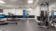 Located at 160 Temple St in New Haven, CT, this single-floor fitness center is thoughtfully designed to accommodate a comprehensive range of workout styles. The space features a clean, modern aesthetic defined by white upper walls accented with a bold black wainscoting detail, recessed and panel lighting, and a drop ceiling that creates a well-lit, functional environment.

The facility is equipped with a strong selection of cardio equipment, including treadmills, elliptical trainers, stationary bikes, and a rowing machine, several of which are outfitted with individual display screens for interactive workout tracking. A dedicated strength training area includes a multi-station cable machine, a rack with a varied dumbbell set, and an assortment of stability and medicine balls for functional training exercises.

Full-length mirrors line multiple walls throughout the space, visually expanding the room and supporting proper form during workouts. The speckled rubber flooring provides traction and impact absorption across the entire area. Additional amenities include a wall-mounted workout guide, a digital fitness kiosk, and paper towel dispensers, ensuring a practical and user-friendly experience for all fitness levels.