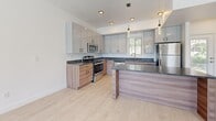 Located in Ogden, Utah, this modern three-story home offers a well-organized layout across its floors, blending contemporary design with functional living spaces. The main level features an open-concept kitchen and living area bathed in natural light from multiple large windows that frame neighborhood views. The kitchen is outfitted with sleek two-tone cabinetry — high-gloss upper cabinets paired with warm wood lower cabinets — dark granite countertops, stainless steel appliances including a refrigerator, range, microwave, and dishwasher, and a peninsula with pendant lighting. Light hardwood-style flooring runs throughout the main living areas, enhancing the bright, airy ambiance. The upper floors house two carpeted bedrooms, including a generously sized primary bedroom with a well-appointed walk-in closet featuring built-in shelving and a hanging rod. Three bathrooms are distributed across the home, each finished with matching warm wood vanities, dark granite countertops, and light flooring. Natural light filters into the bathrooms through windows overlooking greenery. A dedicated entrance, hallway, and multiple staircases ensure smooth circulation throughout all three levels of this clean, move-in-ready home.