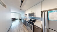 This contemporary 1-bedroom, 1-bathroom unit in Austin, TX (78705) offers a thoughtfully designed open-concept layout that maximizes every square foot of its compact footprint. The galley-style kitchen is outfitted with stainless steel appliances — including an electric range, built-in microwave, and dishwasher — paired with white upper cabinetry, dark lower cabinets, light quartz countertops, and a subtle blue tile backsplash. Track lighting overhead adds a modern touch. Light wood-look flooring runs throughout, creating a cohesive flow into the living area. The living room is a standout, featuring an exposed concrete ceiling and column alongside large floor-to-ceiling windows that flood the space with natural light and offer elevated views of the Austin skyline. The bedroom is cozy and functional, complete with a ceiling fan, a built-in closet, and a high transom window. The bathroom maintains the unit's clean aesthetic with large-format white tile flooring, a wall-mounted vanity with dark cabinetry, a wide mirror, and a minimalist matte-finish door. Throughout the unit, a neutral color palette and modern finishes create a sleek, urban living environment well-suited for Austin's dynamic lifestyle.