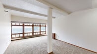 This studio unit at 624 Main Ave in downtown Fargo, ND, is a single-floor space designed for efficient, comfortable living. The open main living area features neutral carpeting, exposed structural beams on a textured ceiling, and a row of large, wood-framed windows along the exterior wall that allow abundant natural light to fill the room. A central support column adds a subtle architectural element to the otherwise open layout, and a baseboard heating system runs along the window wall.

The kitchen is neatly appointed with warm wood cabinetry, a white electric range with overhead ventilation, a stainless steel refrigerator, a dishwasher, and light hardwood-style flooring, offering practical functionality in a compact footprint. A drop-panel ceiling with overhead lighting keeps the kitchen well-lit.

A carpeted hallway connects the living area to the private rooms, featuring a drop-tile ceiling and additional recessed lighting. The bathroom is clean and straightforward, with a full tub/shower combo, white surround, hardwood-style flooring, and open shelving. A closet provides additional storage. The overall ambiance is bright, neutral, and functional, making it a practical urban residence in the heart of Fargo.