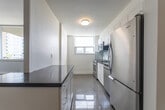 Located at 765 Steeles Ave W in North York, Toronto, this two-bedroom, two-bathroom unit offers a well-organized single-floor layout with a thoughtful mix of living spaces. The combined living and dining area is generously proportioned, featuring classic parquet flooring in a checkerboard pattern and crisp white walls that create a bright, open atmosphere. Structural beam detailing along the ceiling adds architectural character throughout the main living areas.

The kitchen is efficiently designed with a galley-style layout, offering white shaker cabinetry, dark countertops, a light grey subway tile backsplash, and stainless steel appliances including an electric range and refrigerator. Light tile flooring and a window overlooking the surrounding neighbourhood complete the space.

The primary bedroom is spacious and well-lit, benefiting from a large window with views of the cityscape and a baseboard heating system. The second bedroom also features parquet flooring and ample wall space. A dedicated closet and hallway provide practical storage and circulation.

Both bathrooms are finished in a clean, modern style. One features a soaker tub with classic white subway tile surround and chrome fixtures, while the other includes a stone-topped vanity with an undermount sink and large mirror. The overall aesthetic is neutral and move-in ready.