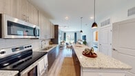 This single-floor residence showcases a thoughtfully designed open-concept layout that seamlessly connects the kitchen, dining, and living areas. The kitchen is a standout feature, equipped with stainless steel appliances, two-tone cabinetry combining light wood uppers with dark lower cabinets, granite countertops, a subway tile backsplash, and a generously sized center island with pendant lighting overhead. Light wood-style flooring runs throughout the main living areas, enhancing the bright, airy atmosphere created by recessed lighting and large windows.

The living area offers a comfortable, modern setting with a sliding glass door that invites natural light and outdoor views. A dedicated bedroom features plush carpeting, a bold accent wall, ceiling fan, ample natural light from a large window, and direct access to an en-suite bathroom. The bathroom is finished with granite countertops, a wood-tone vanity, and a large mirror. An in-unit washer and dryer provide added convenience. The overall design balances contemporary style with functional living, creating a cohesive and welcoming atmosphere throughout.
