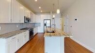 Located at 30 Main in Londonderry, NH, this single-floor residence offers a thoughtfully designed open layout with contemporary finishes throughout. The kitchen serves as a central highlight, featuring a large granite-topped island with an undermount sink, white shaker-style cabinetry, glass-front upper cabinets, a subway tile backsplash, and stainless steel appliances including a range, microwave, and refrigerator with ice maker. Pendant lighting adds a refined touch above the island. The living area is bright and open, with warm hardwood-style flooring and large windows that invite generous natural light and outdoor views. Bedrooms are finished with plush carpeting and feature windows that further enhance the natural light. The primary bathroom is generously sized with tile flooring, a wide vanity with ample cabinetry, a walk-in shower with glass enclosure, and direct access to a walk-in closet with built-in shelving. The secondary bathroom includes a floating vanity, framed mirror, a tall storage cabinet, and a tub-shower combination. A dedicated laundry area with hardwood-style flooring, louvered doors, and washer/dryer hookups rounds out this well-appointed home.