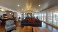 Located in North Little Rock, AR, this single-story home offers a thoughtfully designed open-concept layout that flows seamlessly from room to room. Rich stained concrete floors run throughout, providing a cohesive and durable foundation that complements the warm, rustic aesthetic of the space.

The expansive main living area is anchored by soaring vaulted ceilings and illuminated by a statement orb chandelier, creating an airy and inviting atmosphere. A dramatic floor-to-ceiling stone accent wall serves as a striking architectural focal point between the living and dining areas. Multiple sets of French doors line the exterior walls, flooding the interior with abundant natural light and providing easy access to the outdoors.

The dining area accommodates large gatherings with a substantial wooden table and chairs, set beneath a matching chandelier. A secondary sitting room offers additional flexible space with vaulted ceilings, ample seating, and natural light from multiple windows. A separate, more intimate lounge area features a leather sofa and direct exterior door access.

The kitchen is well-appointed with white upper cabinetry, dark lower cabinetry, granite countertops, a tile backsplash, stainless steel appliances, and a central island with bar seating and pendant lighting overhead — ideal for both cooking and casual dining.