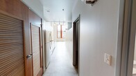 This single-floor unit offers an efficient and thoughtfully designed layout comprising a living area, kitchen, bathroom, and closet space. The interior is defined by polished concrete floors throughout, lending an urban, industrial character that pairs well with the crisp white walls and clean lines found across the space.

The living area is a bright, open room anchored by striking floor-to-ceiling windows with bold red frames, allowing generous natural light to fill the space and offering elevated views of the surrounding cityscape. Track lighting supplements the natural light, ensuring the space remains well-lit throughout.

The kitchen runs along a galley-style corridor and is finished with granite countertops, white cabinetry, and a standout yellow ceramic tile backsplash that adds a vibrant pop of color to the otherwise neutral palette. A stainless steel double-basin sink and full appliance suite complete the functional cooking space.

The bathroom features a clean, white tub-shower combination accented with coordinating yellow tile detailing, maintaining the design cohesion seen throughout the unit.

A dedicated closet area includes a built-in wire shelving and hanging rod system, providing organized and practical storage. The overall ambiance is modern and urban, with carefully chosen design accents that bring personality to a compact yet versatile space.