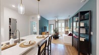 This thoughtfully designed 2-bedroom, 3-bathroom residence offers a functional and stylish single-floor layout. The open-concept living and kitchen area forms the heart of the home, where warm hardwood flooring and bold teal accent walls create a modern yet inviting atmosphere. The kitchen features white cabinetry, stainless steel appliances, a light quartz peninsula with bar seating, and pendant lighting — combining practicality with aesthetic appeal. The living area flows naturally from the kitchen, anchored by a ceiling fan, large windows, and a glass-paned exterior door that fill the space with natural light and views of the outdoors. A tall open shelving unit adds both storage and visual interest to the living room. The primary bedroom is a well-proportioned retreat with hardwood floors, a ceiling fan, large window with patterned drapes, and ample room for furnishings. The second bedroom is equally comfortable, featuring similar finishes and wall art details. Three bathrooms serve the residence, at least one featuring marble-style tile, a soaking tub with shower combination, and refined fixtures. A dedicated walk-in closet with wire shelving provides generous storage. A hallway connects the private areas of the home, completing this efficiently planned and stylishly finished residence.