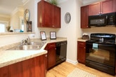 This single-floor residence offers a thoughtfully designed layout with a cohesive neutral color palette throughout. The kitchen is a standout space, featuring rich dark-cherry cabinetry extending to the ceiling, granite-style countertops, a stainless steel sink, and a full suite of black appliances including a range, microwave, dishwasher, and refrigerator. Light hardwood-style flooring and crown molding add a polished finish, while track lighting provides focused illumination.

The open living area flows naturally from the kitchen, highlighted by crown molding, track lighting, and plush carpeting that extends into the bedrooms. Each bedroom benefits from natural light through wide windows with outdoor views of surrounding greenery, and ceiling fans provide added comfort.

The two bathrooms share a consistent design language, each featuring warm tile flooring, rich dark-cherry vanity cabinetry, light countertops, and well-lit mirrors. One bathroom includes an enclosed walk-in shower area with tiled walls, while the other offers a similarly functional layout with a tub-shower combination. Both bathrooms connect conveniently to the adjoining living spaces, contributing to the home's practical and comfortable flow throughout.