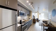 This studio is thoughtfully designed to maximize every square foot of its single-floor layout, blending style and functionality seamlessly. The open-concept plan allows the kitchen, dining, and living areas to flow naturally into one another, creating a cohesive and livable environment.

The kitchen is a standout feature, outfitted with sleek gray cabinetry, dark countertops, and a full suite of stainless steel appliances including a refrigerator, electric range, built-in microwave, and dishwasher. A white subway tile backsplash adds a clean, contemporary touch, while track lighting overhead ensures the space is well-lit and practical.

Light hardwood-style flooring runs throughout, lending warmth and visual continuity across the entire unit. The living area benefits from a large window at the far end, drawing in generous natural light and offering an open, airy feel that enhances the sense of space.

The overall aesthetic is modern and refined, with a neutral color palette of whites, grays, and warm wood tones that creates a calm, inviting atmosphere. The efficient layout makes this studio an ideal space for those seeking contemporary urban living.