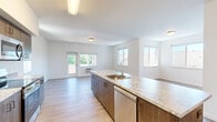 This single-floor, 3-bedroom, 2-bathroom residence offers a thoughtfully designed open-concept layout that maximizes functionality and livability. The kitchen serves as the heart of the home, anchored by a generous island with striking granite-style countertops and an undermount sink. Dark wood cabinetry provides ample storage, while a full suite of stainless steel appliances — including a refrigerator, range, microwave, and dishwasher — completes the space with a modern, cohesive look. The kitchen flows seamlessly into the living area, which is bathed in natural light from multiple windows and a glass-panel door that leads to the outdoors. Light-toned wood-style flooring runs throughout, lending warmth and continuity to the entire residence. The three bedrooms are bright and well-proportioned, each featuring windows with exterior views. The spacious primary bedroom offers a comfortable and private retreat. Both bathrooms are clean and functional, each featuring a tub/shower combination with a white surround, wood-style flooring, and dark wood vanity cabinetry. A dedicated closet provides convenient additional storage. The overall aesthetic is modern and neutral, offering a versatile canvas well-suited to a variety of furnishing styles.