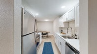 Located at 1518 W Candletree Dr in Peoria, IL, this single-floor, 2-bedroom, 3-bathroom home offers a well-organized and thoughtfully designed layout. The galley-style kitchen is a standout feature, showcasing white shaker cabinetry, gleaming white countertops, a stainless steel sink with a professional-style faucet, and a full suite of stainless steel appliances, including a refrigerator and dishwasher. Light wood-tone flooring runs throughout, lending warmth and continuity to the space. The kitchen flows naturally into a dedicated dining area, which accommodates a striking live-edge wood dining table — a bold design element that anchors the room. The living room provides additional gathering space, complemented by a stylish sideboard and tasteful wall art. The generously sized primary bedroom features a window with natural light, light wood flooring, and a textured ceiling. The second bedroom, currently configured as a home office, also benefits from natural light through its window and includes a closet. Three bathrooms serve the home, each finished with clean white vanities and tile work. Four closets provide ample storage throughout. The neutral color palette, recessed lighting, and consistent use of light wood flooring create a cohesive, modern aesthetic from room to room.