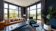 Located at 1 Fineran Way in Short Hills, NJ, this thoughtfully designed single-floor residence offers a seamless blend of modern architecture and refined interior finishes throughout. The living area is a standout feature, boasting dramatic floor-to-ceiling windows on two walls that flood the space with natural light and frame lush, verdant outdoor views. Deep navy accent walls, rich hardwood-style flooring, and a sophisticated color palette create an inviting yet contemporary ambiance. The open-concept kitchen is equipped with gray shaker cabinetry, stainless steel appliances, a generous white quartz waterfall island with seating for multiple guests, and elegant pendant lighting, making it ideal for both everyday living and entertaining. The bedrooms continue the refined aesthetic with large windows offering serene outdoor views, warm wood flooring, and ample space for restful retreats. The primary bathroom features marble-clad shower walls, a glass-enclosed walk-in shower, a dark wood floating vanity with an illuminated mirror, and upscale tile flooring. A separate powder room with marble-look flooring and a pedestal sink provides added convenience. Throughout the residence, high-end finishes, curated design details, and an abundance of natural light define the overall character of this polished Short Hills home.
