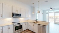Located at 1000 Lakeside Terrace Ct in Wake Forest, NC, this well-appointed single-floor residence offers three bedrooms, two bathrooms, and a thoughtfully designed layout. The kitchen is a standout feature, showcasing crisp white shaker cabinetry adorned with gold hardware, a white subway tile backsplash, light quartz countertops, and a full suite of stainless steel appliances including a range, built-in microwave, dishwasher, and a side-by-side refrigerator with an ice and water dispenser. Pendant lighting with gold accents adds a contemporary touch, while wood-look flooring flows throughout the main living and kitchen areas. The living space connects seamlessly to the kitchen and enjoys access to an outdoor balcony, filling the room with natural light through large windows. The generously sized primary bedroom features plush carpeting, a ceiling fan, and a bank of windows offering views of the surrounding neighborhood. It is complemented by a walk-in closet equipped with multi-tier wire shelving. The bathrooms are finished with white vanities, quartz countertops, matte black fixtures, large framed mirrors, and stylish vanity lighting. Additional bedrooms also feature carpeted floors and closet storage, rounding out a functional and modern living space.