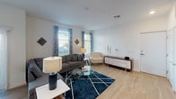 This single-floor space presents a striking industrial-modern aesthetic defined by its signature exposed concrete beam ceilings, which lend architectural character throughout the living areas. The open-concept layout connects the kitchen and living room seamlessly, creating a spacious, airy atmosphere.

The kitchen is well-appointed with stainless steel appliances, including a refrigerator, electric range with overhead microwave, and dishwasher. Two-tone cabinetry pairs dark lower cabinets with white uppers, complemented by a teal subway tile backsplash that adds a vibrant accent. A compact bistro-style island with bar seating provides casual dining space.

The living area benefits from natural light through windows fitted with blinds, while the exposed concrete beams above reinforce the industrial design theme. The neutral flooring and white walls provide a clean backdrop throughout.

The bathroom features a floating dark wood vanity with a light countertop, a large mirror, tile flooring, and a shower-tub combination with curtain enclosure. A dedicated laundry closet houses a full-size stacked washer and dryer unit, adding everyday convenience to this thoughtfully designed space.