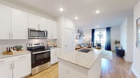 Located in Suwanee, GA, this well-appointed single-floor residence offers a thoughtfully designed open-concept layout that seamlessly connects the kitchen, dining, and living areas. The kitchen is a standout feature, showcasing crisp white shaker cabinetry extending to the ceiling, granite countertops, a large center island with an undermount sink, and a full suite of stainless steel Whirlpool appliances including a French door refrigerator, electric range, and over-the-range microwave. Light hardwood flooring runs throughout the main living spaces, enhancing the bright, airy atmosphere created by recessed lighting overhead. The living room is an inviting retreat, featuring floating wood shelves, a sliding glass door that opens to a private balcony, and an abundance of natural light. The bedroom offers a comfortable, intimate atmosphere with plush carpeting and a bold accent wall. The bathroom continues the clean, modern aesthetic with white cabinetry, granite countertops, a large vanity mirror, and a tub-shower combination finished with subway tile surround. A dedicated laundry room houses a full-size top-load washer and dryer with built-in wire shelving for added storage. This residence delivers a cohesive, contemporary design throughout.