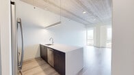 Located in Chicago's vibrant Old Town neighborhood, this contemporary residence at 1365 N Sedgwick St showcases a refined modern design highlighted by striking exposed concrete ceilings that lend an industrial-chic character throughout. Light wood-tone flooring flows seamlessly across the open-plan layout, complementing the crisp white walls and creating a bright, cohesive aesthetic.

The kitchen serves as a central focal point, featuring a large peninsula with sleek light-colored countertops, an undermount sink, and rich dark wood cabinetry. Stainless steel appliances — including a French door refrigerator, gas range, and dishwasher — are complemented by a suspended linear pendant light that adds a contemporary accent.

The living and sleeping areas are generously proportioned, each benefiting from floor-to-ceiling windows that flood the interior with natural light and frame expansive views of the Chicago skyline and surrounding neighborhood rooftops. Built-in closet storage and a dedicated workspace nook provide practical functionality.

The bathroom is finished to a high standard, featuring a glass-enclosed shower, a dual-sink vanity with white countertops atop bold blue cabinetry, and large-format white tile flooring. Together, these elements create a clean, modern space well-suited to urban living.