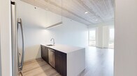 Located in Chicago's vibrant Old Town neighborhood, this contemporary residence at 1365 N Sedgwick St showcases a refined modern design highlighted by striking exposed concrete ceilings that lend an industrial-chic character throughout. Light wood-tone flooring flows seamlessly across the open-plan layout, complementing the crisp white walls and creating a bright, cohesive aesthetic.

The kitchen serves as a central focal point, featuring a large peninsula with sleek light-colored countertops, an undermount sink, and rich dark wood cabinetry. Stainless steel appliances — including a French door refrigerator, gas range, and dishwasher — are complemented by a suspended linear pendant light that adds a contemporary accent.

The living and sleeping areas are generously proportioned, each benefiting from floor-to-ceiling windows that flood the interior with natural light and frame expansive views of the Chicago skyline and surrounding neighborhood rooftops. Built-in closet storage and a dedicated workspace nook provide practical functionality.

The bathroom is finished to a high standard, featuring a glass-enclosed shower, a dual-sink vanity with white countertops atop bold blue cabinetry, and large-format white tile flooring. Together, these elements create a clean, modern space well-suited to urban living.