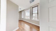 Located in the heart of downtown Rochester, this well-appointed 2-bedroom, 5-bathroom residence on the 11th floor offers a thoughtfully designed single-level layout with generous living space. The open living room is a standout, featuring gleaming hardwood floors and a bank of large windows fitted with blinds that frame sweeping city skyline views, flooding the room with natural light.

The modern kitchen is outfitted with contemporary wood-grain cabinetry, white quartz countertops, a subway tile backsplash, stainless steel appliances — including a gas range, microwave, dishwasher, and side-by-side refrigerator — and track lighting overhead. Hardwood flooring continues seamlessly throughout the main living areas.

The spacious primary bedroom features plush carpeting and direct hallway access to the rest of the unit. Five well-designed bathrooms serve the residence; bathrooms include clean tile flooring, wood-grain vanities with white countertops, framed mirrors, and glass-enclosed shower stalls. One bathroom features a pedestal sink and accessibility grab bar.

A dedicated laundry room houses a full-size, front-loading washer and dryer with overhead shelving for added storage convenience. Neutral tones, clean lines, and modern finishes throughout create a cohesive, contemporary ambiance well-suited for urban living.