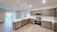 Located at 900 Third St SE in Cedar Rapids, Iowa, this well-appointed 3-bedroom, 2-bathroom unit offers a thoughtfully designed single-floor layout ideal for comfortable everyday living. The open-concept kitchen serves as the heart of the home, featuring taupe shaker-style cabinetry, crisp white countertops, a peninsula with an undermount sink, and a full suite of stainless steel appliances including a refrigerator, range, built-in microwave, and dishwasher. Stylish pendant lighting illuminates the kitchen and peninsula, complemented by recessed ceiling lights throughout. Light-toned luxury vinyl plank flooring runs through the main living and kitchen areas, lending a clean, contemporary feel. The primary bedroom is generously sized and includes a walk-in closet outfitted with wire shelving for ample organization. All bedrooms feature soft carpeting and large windows that allow natural light to fill each room, with urban views of the surrounding Cedar Rapids cityscape. The two bathrooms are finished with matching wood-toned vanities, white countertops, large mirrors, and light-wash LVP flooring. One bathroom includes a walk-in shower. A hallway connects the bedrooms and shared spaces, completing this efficient and modern floor plan.
