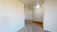 This single-floor residence at 7873 W Mansfield Pkwy in Lakewood, Colorado offers a straightforward, functional layout designed for comfortable everyday living. The living area is finished with neutral-toned carpet and features a ceiling fan with a light fixture overhead. A wood-toned entry foyer transitions seamlessly into the carpeted main space, and a large window allows natural light to fill the room, offering views of the surrounding neighborhood.

The kitchen is equipped with warm honey-toned wood cabinetry providing ample storage above and below the countertops. White appliances, including a freestanding electric range and a full-size refrigerator, are neatly integrated into the layout. Wood-style vinyl flooring runs throughout the kitchen, complementing the cabinetry tones. A partial dividing wall separates the kitchen from the adjacent living space.

The bedroom is generously sized with soft carpeting, a closet, and direct access to the hallway. The bathroom features wood-style flooring, a vanity with wood-accented cabinetry, a wall mirror illuminated by a bar light fixture, and a combined tub and shower. The overall palette throughout the unit is light and neutral, contributing to a clean, welcoming ambiance.