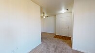 This single-floor residence at 7873 W Mansfield Pkwy in Lakewood, Colorado offers a straightforward, functional layout designed for comfortable everyday living. The living area is finished with neutral-toned carpet and features a ceiling fan with a light fixture overhead. A wood-toned entry foyer transitions seamlessly into the carpeted main space, and a large window allows natural light to fill the room, offering views of the surrounding neighborhood.

The kitchen is equipped with warm honey-toned wood cabinetry providing ample storage above and below the countertops. White appliances, including a freestanding electric range and a full-size refrigerator, are neatly integrated into the layout. Wood-style vinyl flooring runs throughout the kitchen, complementing the cabinetry tones. A partial dividing wall separates the kitchen from the adjacent living space.

The bedroom is generously sized with soft carpeting, a closet, and direct access to the hallway. The bathroom features wood-style flooring, a vanity with wood-accented cabinetry, a wall mirror illuminated by a bar light fixture, and a combined tub and shower. The overall palette throughout the unit is light and neutral, contributing to a clean, welcoming ambiance.