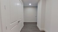 This single-story home offers a clean, contemporary design across a generously sized floor plan housing three bedrooms, two bathrooms, a combined kitchen and living area, and a connecting hallway. Consistent wood-look plank flooring flows throughout every room, contributing to a cohesive, modern aesthetic complemented by crisp white walls and clean baseboards.

The kitchen features bold navy-blue cabinetry paired with light countertops, stainless steel appliances including a refrigerator and range, and recessed lighting overhead. It opens directly into the living area, which benefits from multiple windows fitted with horizontal blinds and a ceiling fan, creating a bright and airy atmosphere.

The primary bedroom is a well-proportioned retreat with natural light from large windows and access to an ensuite bathroom. This bathroom includes a dual-sink dark vanity with a light countertop, a framed mirror, and a tiled shower. An adjacent walk-in closet features built-in shelving and hanging rods for organized storage.

The secondary bathroom includes a glass-enclosed tiled shower, a dark vanity, and a grab bar. Additional bedrooms are bright and functional, with one offering notable natural light through large windows. Three closets total provide practical storage throughout the home.