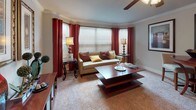 The Liberty is a well-appointed one-bedroom, one-bathroom residence laid out on a single floor, offering a comfortable and cohesive living experience throughout. The living room serves as the heart of the home, featuring plush carpeting, crown molding, and a ceiling fan. A large bay window arrangement dressed with bold red curtains and horizontal blinds floods the space with natural light, creating a warm and inviting atmosphere. The kitchen is efficiently designed with warm oak cabinetry, ample counter space, and full appliances including a coil-burner range, over-the-range microwave, and dishwasher. Tile flooring adds practicality to this functional cooking space. The bedroom is a restful retreat complete with soft carpeting, a ceiling fan with light fixture, and a window with blinds and curtains that allow for adjustable light control. Decorative wall art and thoughtful accents contribute to the room's cozy ambiance. The full bathroom features tile flooring, a tub and shower combination enclosed by elegant patterned curtains, a vanity with oak cabinetry, and ample storage. Overall, the Liberty floor plan delivers a functional, comfortable, and well-designed living space suited for everyday living.
