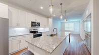 Located at 3250 Buford Hwy in Duluth, GA, this contemporary single-floor residence offers a well-designed open layout with modern finishes throughout. The kitchen serves as a central highlight, showcasing an expansive granite island with an undermount sink, crisp white shaker cabinets, a classic subway tile backsplash, and a full suite of stainless steel appliances including a side-by-side refrigerator, electric range, and built-in microwave. Sleek cylindrical pendant lights hang above the island, adding a refined touch. The kitchen flows seamlessly into the living area, which features warm hardwood-style flooring and access to an exterior door with natural light filtering through blinds. The bedrooms are carpeted for comfort, each equipped with a ceiling fan and windows offering natural light and outdoor views. The primary bathroom includes granite countertops, a single undermount vanity sink, tile flooring, and direct access to a spacious walk-in closet with built-in shelving. Additional carpeted rooms provide versatile living or sleeping spaces. The overall aesthetic is clean, bright, and contemporary, with neutral tones and quality finishes creating a cohesive and inviting atmosphere throughout.