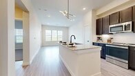 Located in Grand Prairie, TX, this thoughtfully designed one-bedroom, one-bathroom residence offers a modern living experience across a single floor. The open-concept layout seamlessly connects the kitchen and living room, creating a bright and airy atmosphere enhanced by light wood-style flooring and neutral tones throughout.

The kitchen is a standout feature, boasting rich dark cabinetry, a white subway tile backsplash, granite countertops, and a central island with an undermount sink and matte black faucet. Stainless steel appliances, including a refrigerator, dishwasher, and microwave, complete this well-appointed space. A striking multi-arm brass pendant light adds a stylish focal point overhead.

The living room is bathed in natural light from large windows that frame outdoor views, with light-toned flooring continuing the clean, cohesive aesthetic. The bedroom offers plush carpeting, generous natural light through wide windows with outdoor views, and a dedicated closet for storage.

The bathroom features dark vanity cabinetry with granite countertops, a large framed mirror, and a tiled shower-tub combination with matte black fixtures. A hallway connects the living areas to the private spaces, ensuring a practical and functional flow throughout this well-designed home.