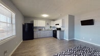 This single-story unit offers a practical and well-designed layout that maximizes its compact footprint. The open-concept living and kitchen area serves as the heart of the space, where wood-style laminate flooring extends throughout, creating a cohesive and easy-to-maintain foundation. The walls are painted in a cool, neutral gray tone that complements the overall aesthetic and provides a clean, modern backdrop.

The kitchen is functionally equipped with two-tone cabinetry — white upper cabinets paired with gray lower cabinets — and granite-style countertops. Black appliances, including a refrigerator and range, provide a bold contrast. A window above the sink area allows for natural light. The living area flows seamlessly from the kitchen and is generously proportioned, with a front entry door and a window that brings in additional natural light.

The bedroom is a comfortable, private space featuring a ceiling fan with light fixture, a window for ventilation and natural light, and access to a closet. The textured ceilings are present throughout the unit.

The bathroom includes a tub/shower combination with large-format dark tile surround, adding a striking design element. A window provides natural light and ventilation, completing this efficiently designed unit.