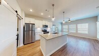 Located in La Porte, TX, this well-appointed single-story home offers three bedrooms and two bathrooms within a thoughtfully designed open-concept floor plan. The combined kitchen and living area forms the heart of the home, featuring warm wood-look flooring, recessed lighting, and a ceiling fan that enhances comfort and airflow. The kitchen is a standout, showcasing white shaker cabinetry, a subway tile backsplash, stainless steel appliances including a refrigerator with ice maker, electric range, and built-in microwave, all centered around a spacious quartz-topped island with a undermount sink and elegant pendant lighting. A sliding barn door leads to a dedicated laundry room conveniently adjacent to the kitchen. The primary bedroom is generously sized and features a walk-in closet with built-in shelving and hanging rods. Additional bedrooms offer plush carpeting and ample natural light from multiple windows. The bathrooms are clean and functional, featuring white vanities and a tub-shower combination. A large pantry with floor-to-ceiling shelving provides abundant storage. Neutral tones and modern fixtures throughout create a bright, cohesive aesthetic suited for comfortable everyday living.