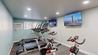 Located at 131 W 200 N in Salt Lake City, Utah, this fitness center offers a well-appointed, single-floor layout thoughtfully divided into distinct workout zones. The space is finished with a clean, modern aesthetic, featuring soft teal and neutral gray walls, recessed lighting throughout, and a combination of rubber gym flooring and light wood-look flooring in transitional areas.

The main cardio zone is equipped with incline treadmills and spin bikes, accompanied by wall-mounted flat-screen TVs to keep workouts engaging. Natural light filters in through multiple windows fitted with blinds, complementing the bright recessed lighting overhead.

A connected strength training area houses a full dumbbell rack with a wide range of weights, adjustable workout benches, and a large wall mirror that enhances the sense of space and allows for form-checking during exercises. This area also features a wall-mounted TV, adding to the functionality of the room.

The layout includes an additional room with light hardwood-style flooring, accessible via interior doors with classic panel detailing, suitable for stretching or supplementary fitness activities. A sanitation station is also present, underscoring the facility's attention to cleanliness. Overall, the fitness center provides a comprehensive and comfortable environment for a full range of workout routines.