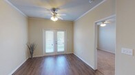 This single-story, 3-bedroom, 2-bathroom home offers a thoughtfully designed open floor plan with a warm, neutral color palette throughout. Rich hardwood-style flooring flows through the main living areas, complemented by crown molding and ceiling fans that add a polished touch to every room.

The spacious living area is anchored by a ceiling fan and opens to a private balcony through elegant French doors, allowing natural light to pour in. Adjacent to the living space, a dedicated dining area features a modern pendant light fixture and seamlessly connects to the kitchen.

The kitchen is well-appointed with dark espresso cabinetry, granite-look countertops, and a full suite of black appliances including a refrigerator, electric range, built-in microwave, and dishwasher. Hardwood-style flooring and a breakfast bar enhance the kitchen's functionality and style.

The bedrooms are carpeted for comfort. The primary bedroom includes a generous walk-in closet with multi-level shelving and hanging rods. Secondary bedrooms feature double-door closets with ample storage. Both bathrooms are finished with dark cabinetry, white countertops, wood-look flooring, and bright vanity lighting with large mirrors, creating a clean and contemporary feel throughout.