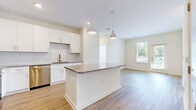 Located at 13511 Montoy Way in Charlotte, NC, this single-floor, three-bedroom, two-bathroom home offers a thoughtfully designed layout with modern finishes throughout. The open-concept kitchen serves as the heart of the home, showcasing crisp white shaker cabinetry, granite countertops, a central island with pendant lighting, stainless steel appliances including a refrigerator, range, microwave, and dishwasher, and a subway tile backsplash. Light wood-tone LVP flooring flows seamlessly from the kitchen into the adjacent living area, which is filled with natural light from a large window. The three bedrooms feature neutral carpet, bright windows with views of the surrounding greenery, and generous closet space. The primary bedroom is served by an en-suite bathroom with a dual-sink granite vanity, white cabinetry, a walk-in shower, and direct access to a spacious walk-in closet outfitted with wire shelving. The secondary bathroom mirrors the same clean, contemporary aesthetic. Two hallways connect the living spaces efficiently, while two closets provide ample storage. The home's neutral color palette and modern fixtures create a bright, clean, and move-in-ready atmosphere throughout.