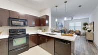Located in Houston's vibrant Washington Avenue corridor, this 1-bedroom, 2-bathroom unit offers a thoughtfully designed layout with modern finishes throughout. The open-concept kitchen flows seamlessly into the combined dining and living area, creating a connected, functional space ideal for everyday living. The kitchen is outfitted with rich dark-wood cabinetry, white countertops, black appliances including a refrigerator, range, microwave, and dishwasher, and a peninsula with pendant lighting overhead. Light tile flooring anchors the kitchen and entry areas. The living room features wood-look flooring, a large window that invites natural light, and neutral walls that complement a variety of décor styles. The bedroom is a comfortable retreat with plush carpet, ample natural light, and access to a generously sized walk-in closet equipped with wire shelving on multiple walls. The two bathrooms include a full tub-shower combination with tile surround. A dedicated in-unit laundry closet houses a full-size washer and dryer with overhead shelving for added storage. A hallway connects the living areas to the private bedroom wing, maintaining a clear and efficient flow throughout this well-appointed Houston residence.