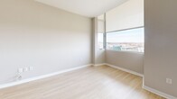 This well-appointed 2-bedroom, 2-bathroom unit at 6445 America Blvd in Hyattsville, MD offers a thoughtfully designed open-concept layout across a single floor. The living room is bright and airy, featuring light wood flooring, neutral tones, and large floor-to-ceiling windows that flood the space with natural light and offer sweeping views of the surrounding skyline and landscape. A ceiling-mounted HVAC unit ensures year-round comfort. The kitchen is modern and functional, equipped with stainless steel appliances including an electric range, microwave, and refrigerator, complemented by white cabinetry, a tile backsplash, light countertops, and a peninsula with a sink — ideal for both cooking and casual dining. The two bedrooms offer distinct finishes: one features light wood flooring and expansive windows with outdoor views, while the primary bedroom is carpeted, generously sized, and connects to a dedicated closet and bathroom. Both bathrooms are clean and contemporary; the primary bath includes a glass-enclosed walk-in shower, backlit vanity mirror, and white tile flooring. Three closets provide ample storage throughout. A dedicated laundry area adds everyday convenience, rounding out this well-organized and modern living space.