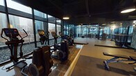 Located at 668 N La Salle Dr in Chicago's River North neighborhood, this fitness center is designed to offer a comprehensive workout environment with a sleek, industrial aesthetic. The space features an exposed dark ceiling with pendant lighting, floor-to-ceiling glass windows along multiple walls, and a combination of polished tile and rubberized flooring that defines distinct workout zones.

The cardio section is lined along the window-facing perimeter, housing Life Fitness treadmills, ellipticals, and stair climbers, each positioned to take full advantage of sweeping views of the Chicago skyline and surrounding urban landscape. Natural light filters in generously throughout the day, enhancing the open, airy feel of the space.

A separate strength and functional training area features rubber flooring, a squat/power rack with weight plates, adjustable benches, a dumbbell rack, and TRX suspension trainers anchored to the ceiling. Glass partitions divide the zones while maintaining visual connectivity throughout. Floor-to-ceiling mirrors expand the sense of space and support proper form during training.

The overall ambiance is modern and performance-oriented, blending urban sophistication with a well-appointed, multi-functional layout suited for a wide range of fitness routines.