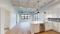 Located at 349 E Main Ave in Zeeland, MI, this thoughtfully designed single-floor unit offers a bright, modern living experience across six well-appointed spaces. The open-concept layout connects the kitchen and living area seamlessly, creating a spacious, airy feel enhanced by soaring ceilings with exposed white-painted wood beams and structural elements that lend an industrial-chic character throughout.

The kitchen is a standout feature, outfitted with crisp white shaker cabinetry, a slate-blue subway tile backsplash, stainless steel appliances including a refrigerator, range, and microwave, and a large central island with a white quartz countertop and undermount sink. Stylish black pendant lights hang above, adding a modern finishing touch.

The living area is bathed in natural light from large black-framed windows and a dramatic floor-to-ceiling glass sliding door that opens directly onto a private balcony, offering views of the surrounding Zeeland neighborhood. Light-toned luxury vinyl plank flooring runs throughout the main living spaces, while the bathroom features clean porcelain tile, white cabinetry with matte black hardware, and a sleek vanity. Additional rooms provide flexible, well-lit spaces with neutral tones and clean finishes, completing this polished and contemporary residence.