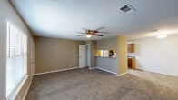 This single-story residence in Biloxi, Mississippi offers a well-designed layout that maximizes functionality throughout. The living area is generously proportioned, featuring neutral-toned carpet, warm beige walls, a textured ceiling, and a ceiling fan with integrated lighting. A pass-through counter connects the living space to the kitchen, creating an open feel while maintaining clear definition between areas.

The galley-style kitchen is a standout feature, equipped with rich wood cabinetry, granite-style countertops, and stainless steel appliances including a refrigerator, electric range, built-in microwave, and dishwasher. A double basin sink and skylight-style overhead lighting enhance the kitchen's practicality. Just beyond the kitchen, a dedicated laundry area houses a full-size washer and dryer.

The bedroom is comfortably sized with carpeted flooring, a ceiling fan, natural light from a window with blinds, and the notable convenience of two separate closets with rod storage. The bathroom features wood-look flooring, a vanity with a white countertop, a mirror, shower, and grab bars for added accessibility. White trim and clean lines throughout contribute to a cohesive, functional ambiance.
